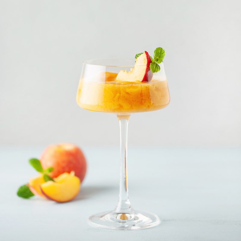Captivating image of a Peach Bellini cocktail elegantly served in a champagne flute, adorned with fresh mint leaves and apple slices. A delightful blend of peach nectar and sparkling wine, creating a visually stunning and flavorful beverage experience.